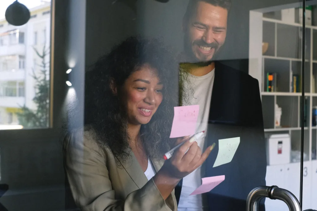 Diverse happy business partners checking stickers on glass door and smiling together in office. small affectionate gestures could be subtle signs a coworker likes you or a colleague has feelings for you.