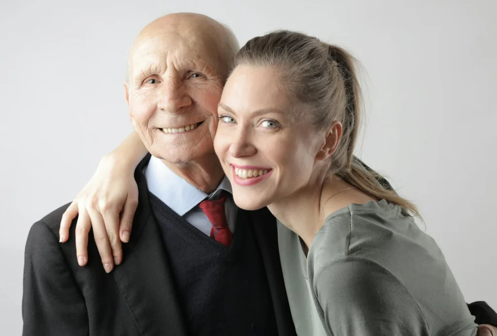 Cheerful elderly man and adult woman cuddling on white background and looking at camera. Attracted to older men, romantic attraction. 