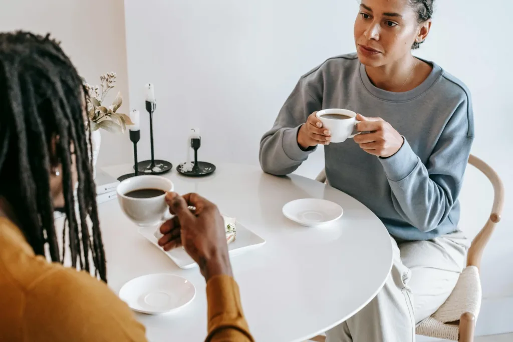 From above of crop pensive Hispanic female in casual clothes sitting at light table and drinking coffee with African American boyfriend in modern cafe. Conflict resolution, romantic relationship