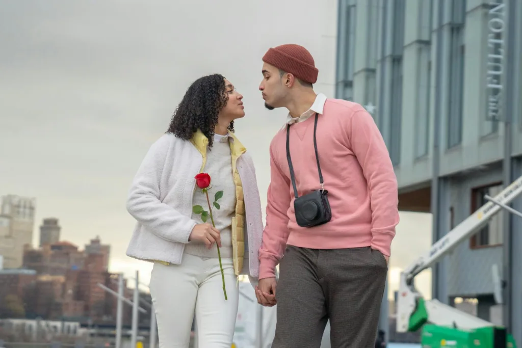 Loving Hispanic girlfriend with flower and boyfriend with photo camera holding hands and looking at each other while strolling on street. Managing expectations, Romantic partnership