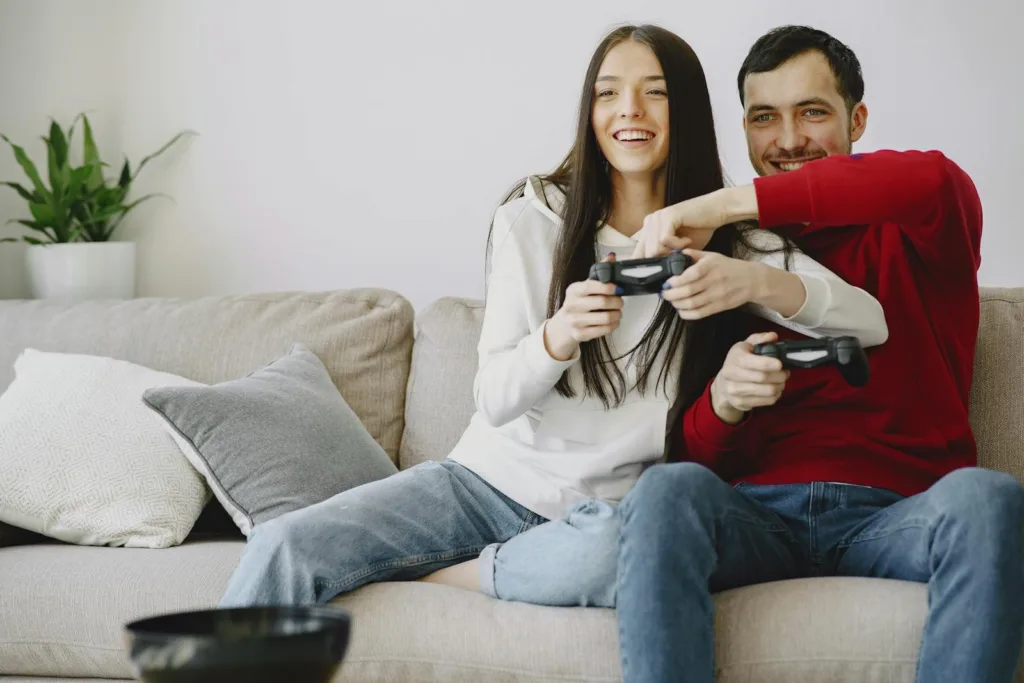 Joyful female and male in casual clothes sitting on comfortable sofa in living room while laughing and playing video game. Nurturing Passion, Long-term relationship