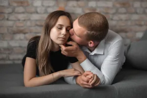 Young Man and Woman Holding Hands and Man Kissing Her in Cheek