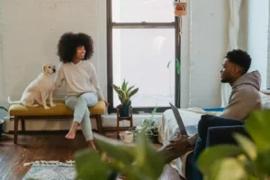 Joyful young African American woman sitting on bench with loyal dog and chatting with boyfriend working remotely on laptop at home