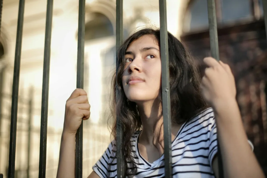 Sad isolated young woman looking away through fence with hope. Manifesting your dream relationship, emotional strength