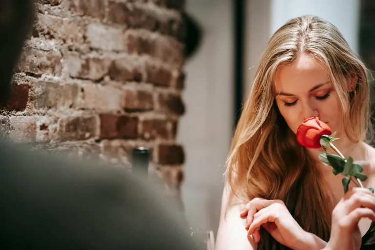 Young couple in elegant clothes in light cafeteria near brick wall having romantic dinner while smelling red rose. God’s Will, Romantic Relationship