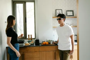 Young Asian man with vision loss in black glasses standing in kitchen with wife preparing breakfast while spending morning together at home. Overcoming obstacles, passion in a marriage